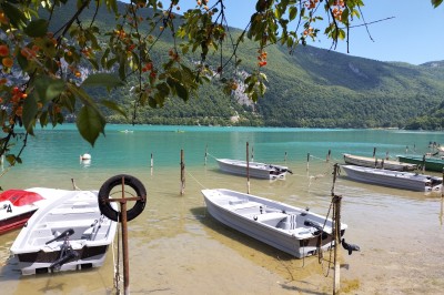 Voilier blanc amarré sur un lac calme, entouré de montagnes verdoyantes sous un ciel dégagé.
