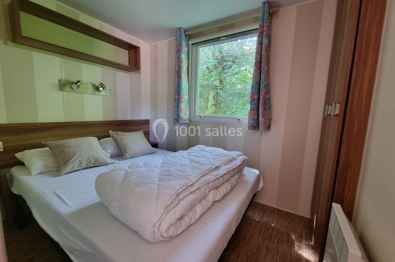 Chambre lumineuse avec lit double, couette pliée, oreillers, fenêtre donnant sur un jardin arboré.