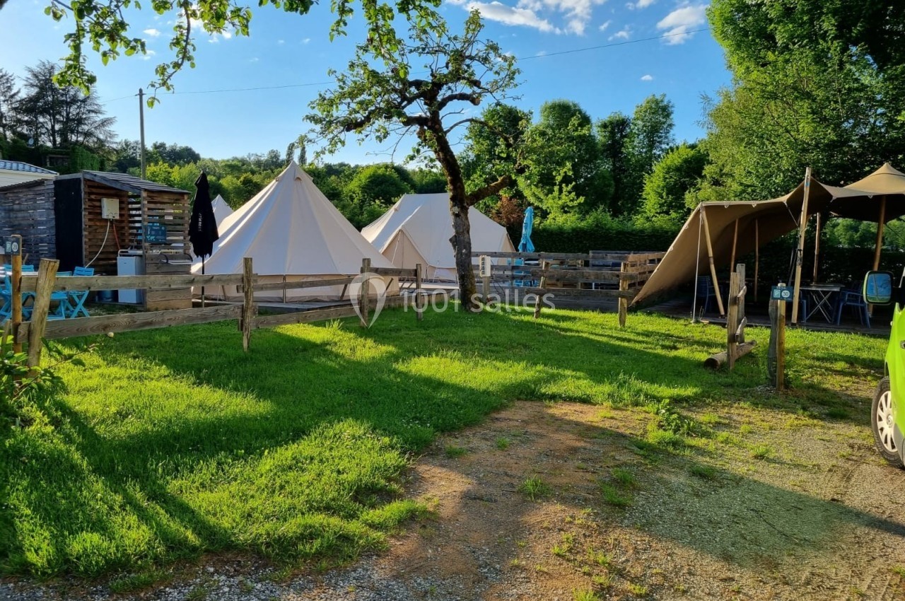 Tentes blanches installées dans un espace verdoyant avec arbres, clôtures en bois et mobilier extérieur.