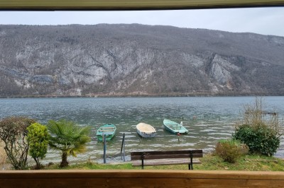 Voilier blanc amarré sur un lac calme, entouré de montagnes verdoyantes sous un ciel dégagé.
