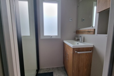 Voilier blanc amarré sur un lac calme, entouré de montagnes verdoyantes sous un ciel dégagé.