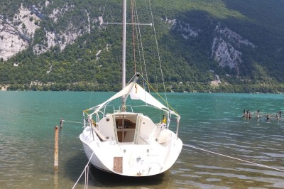 Voilier blanc amarré sur un lac calme, entouré de montagnes verdoyantes sous un ciel dégagé.