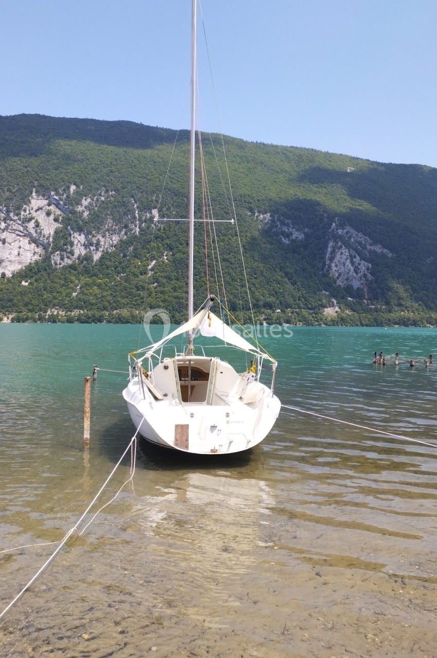Voilier blanc amarré sur un lac calme, entouré de montagnes verdoyantes sous un ciel dégagé.