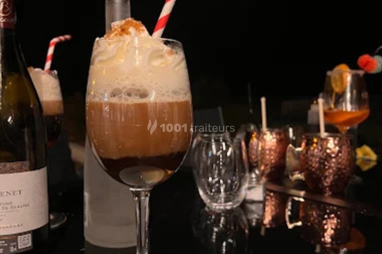 Verres de cocktails garnis de crème fouettée sur une table sombre, entourés de bouteilles et d'autres boissons.