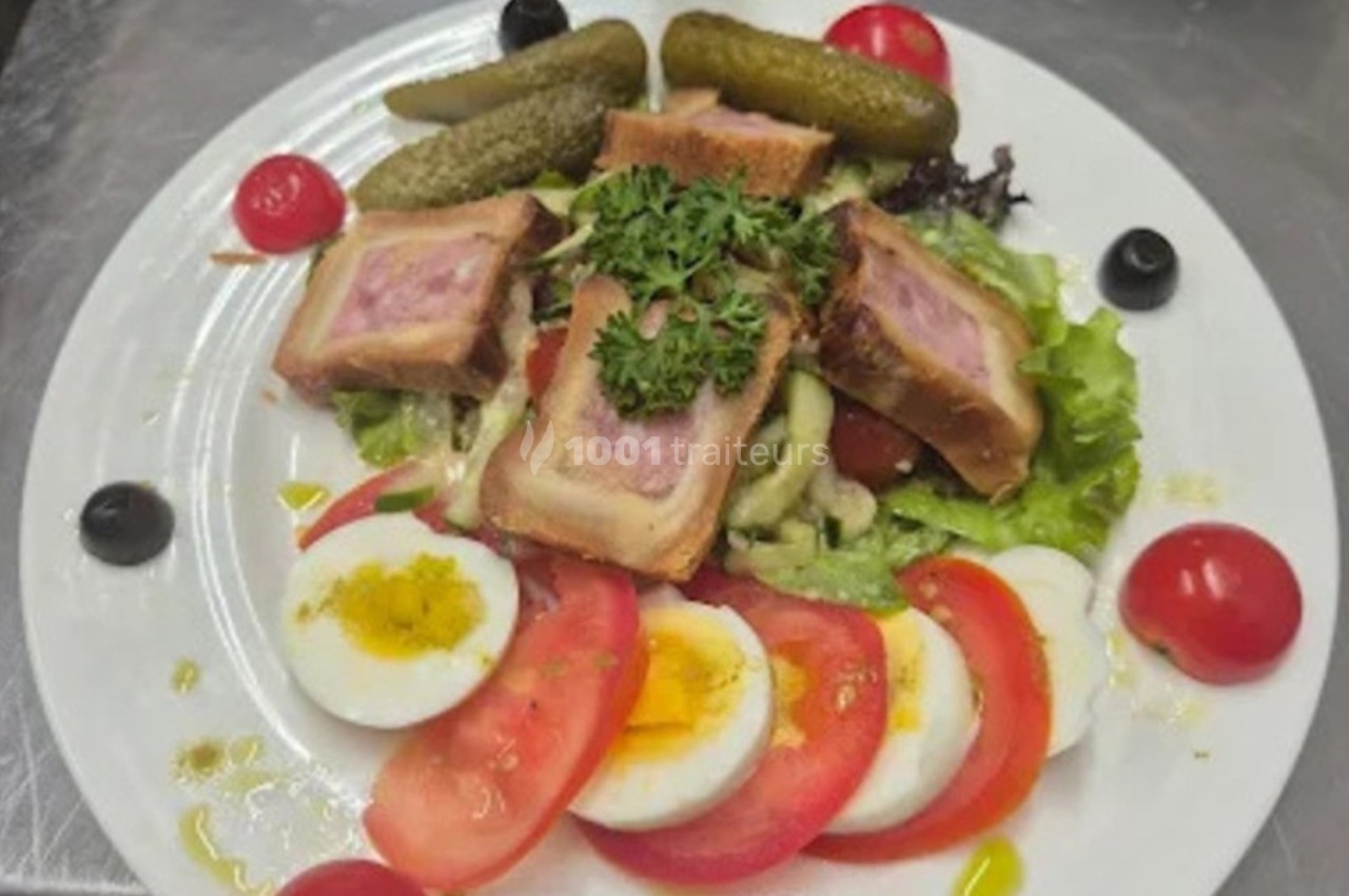 Assiette composée de pâté en croûte, œufs durs, tomates, cornichons, olives et salade verte, garnie de persil.