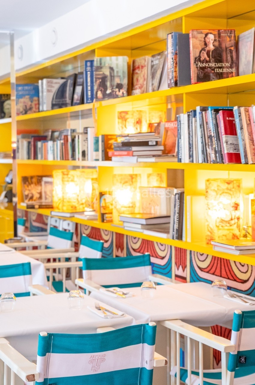 Salle de restaurant lumineuse avec étagères jaunes remplies de livres et tables dressées avec chaises pliantes.