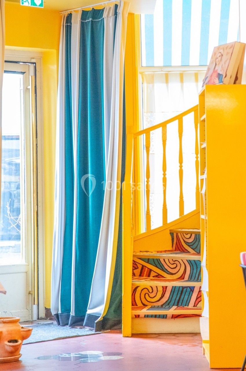 Escalier coloré en bois avec motifs, entouré de murs jaunes, rideaux bleus et mobilier lumineux dans un intérieur.