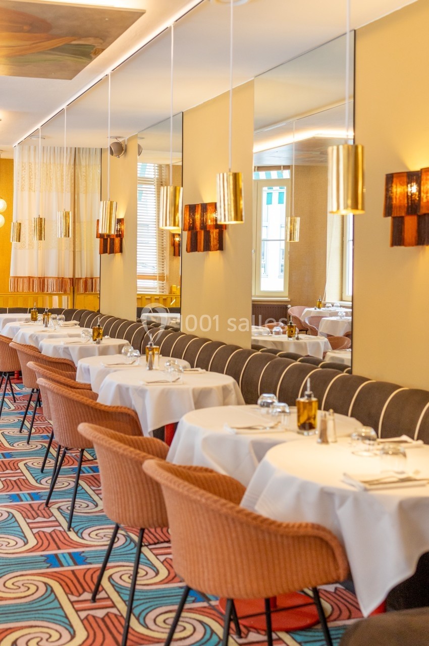 Salle de restaurant élégante avec tables dressées, chaises en velours, miroirs muraux et luminaires suspendus.