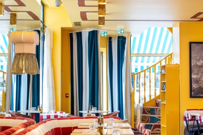 Miniature Location salle Lille (Nord) - Pizza Armand #7 Salle de restaurant lumineuse avec tables dressées, banquettes rayées rouges et blanches, et décor coloré.