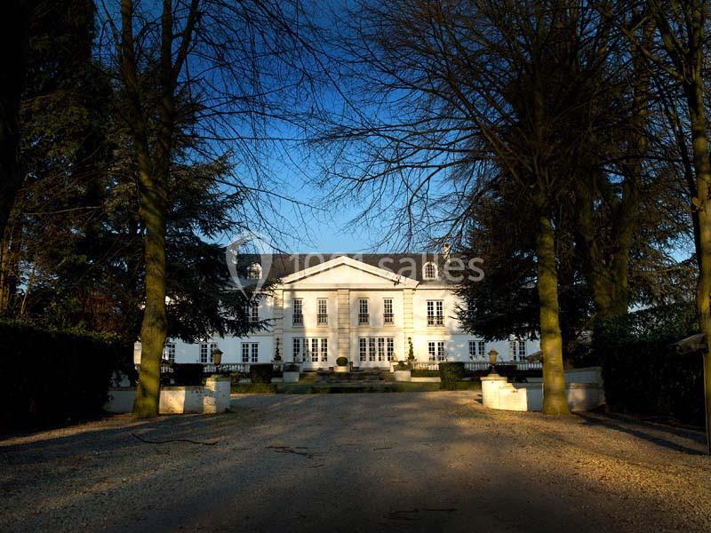 Allée bordée d'arbres menant à un grand bâtiment blanc de style classique sous un ciel dégagé.