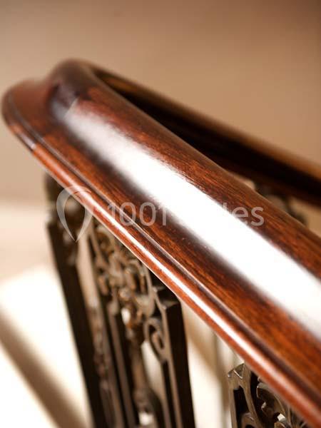 Rampe d'escalier en bois verni avec des balustres en métal ornés de motifs décoratifs.