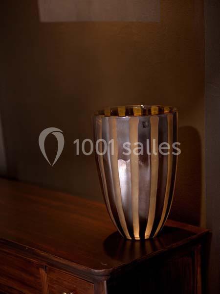 Vase décoratif en verre rayé doré et brun posé sur un meuble en bois sombre dans un intérieur tamisé.