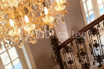 Lustre en cristal allumé suspendu au-dessus d'un escalier avec rampe en fer forgé et sol en marbre.