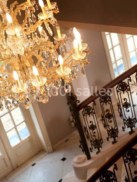 Lustre en cristal allumé suspendu au-dessus d'un escalier avec rampe en fer forgé et sol en marbre.