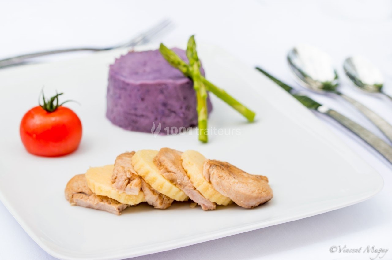 Assiette contenant des tranches de viande, une purée violette, des asperges vertes et une tomate cerise.