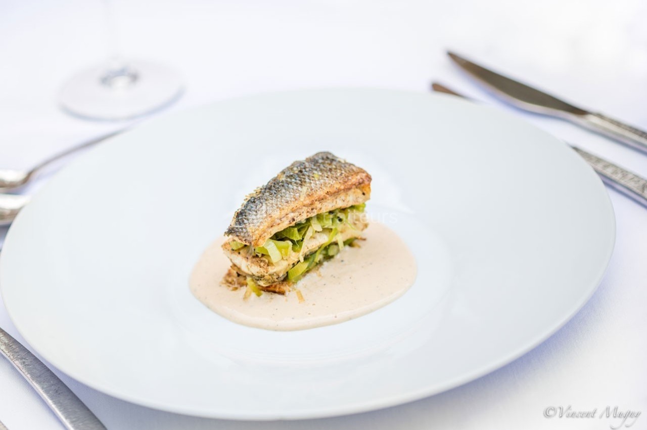 Filet de poisson grillé servi sur un lit de légumes avec une sauce crémeuse, présenté dans une assiette blanche.