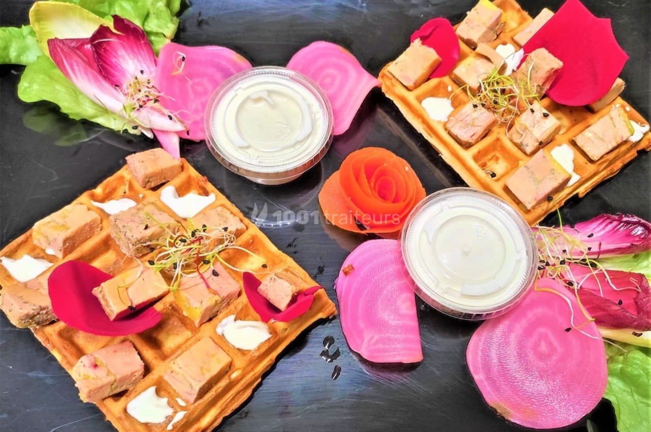 Assiette de gaufres garnies de foie gras, pétales de rose, betteraves et sauces, présentée sur un plateau noir.