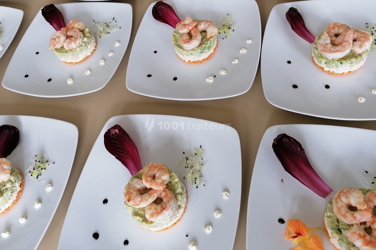 Assiettes dressées avec des entrées composées de crevettes, mousse d'avocat, et décoration de feuilles et fleurs comestibles.