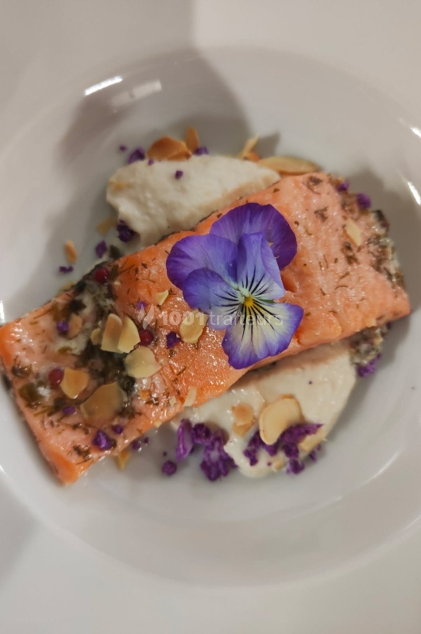 Filet de saumon garni d'une fleur comestible, amandes effilées et purée, présenté dans une assiette blanche.