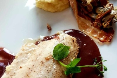 Filet de poisson avec sauce au vin rouge, purée, lard croustillant et garniture de champignons sur une assiette blanche.