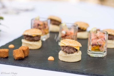 Mini-burgers, verrines de tartare et cubes panés disposés sur une ardoise noire, présentés pour un apéritif.