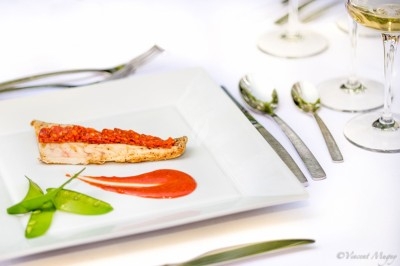 Assiette gastronomique avec tranche de poisson, purée rouge, pois gourmands et couverts sur une table dressée.