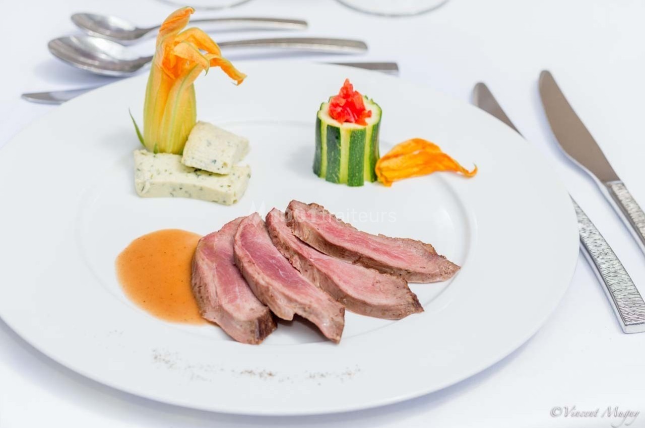 Assiette gastronomique avec tranches de viande, sauce, courgette farcie et fleur comestible en décoration.