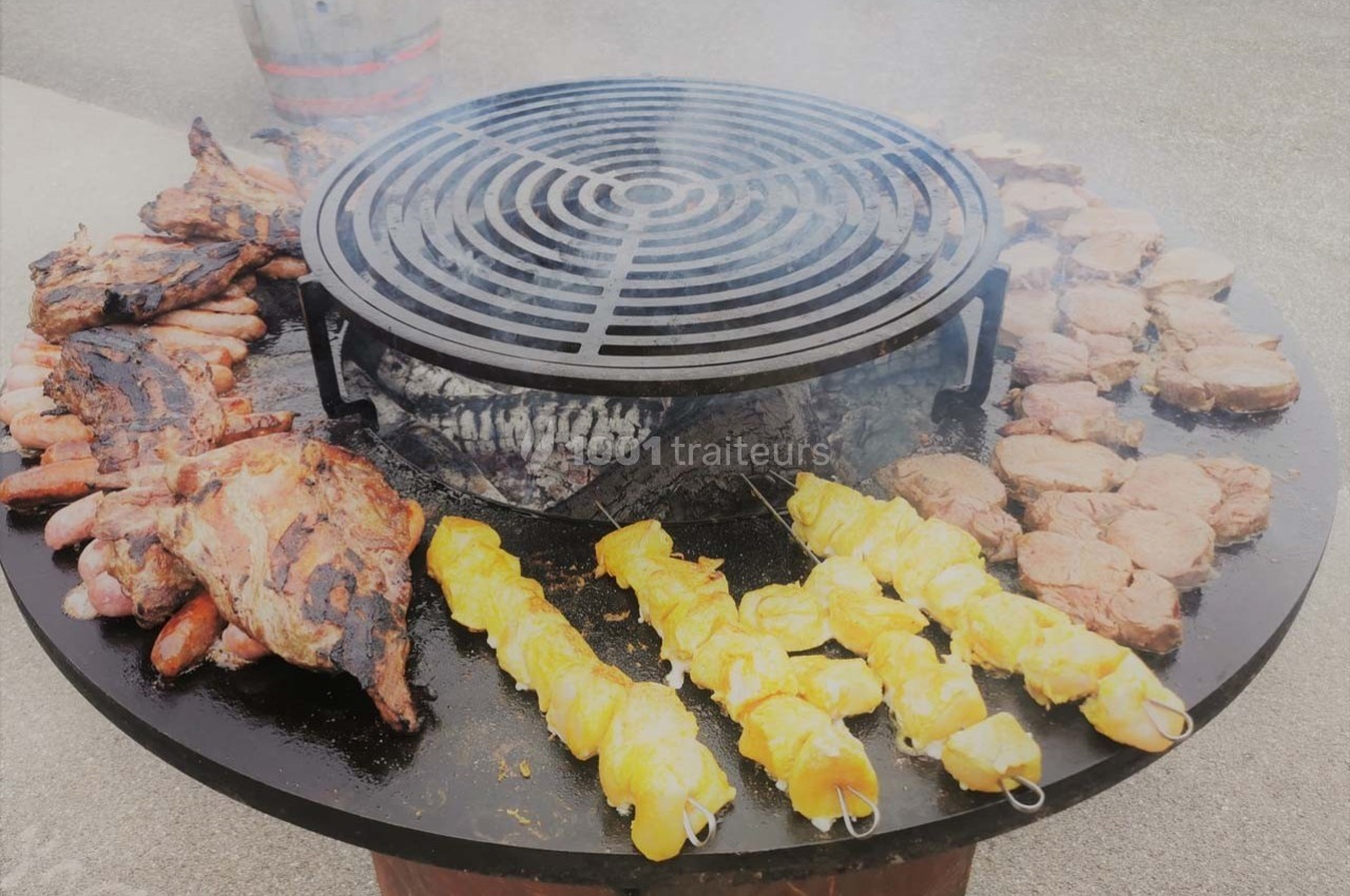 Grill circulaire avec diverses viandes en cuisson, dont brochettes de poulet, saucisses et côtes.