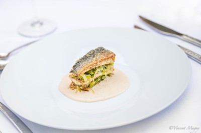 Plateau de fromages variés entourés de grappes de raisin, noix et herbes fraîches sur une table claire.