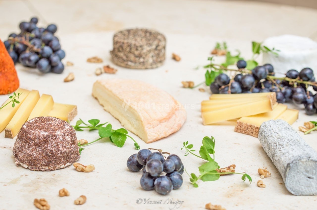 Plateau de fromages variés entourés de grappes de raisin, noix et herbes fraîches sur une table claire.