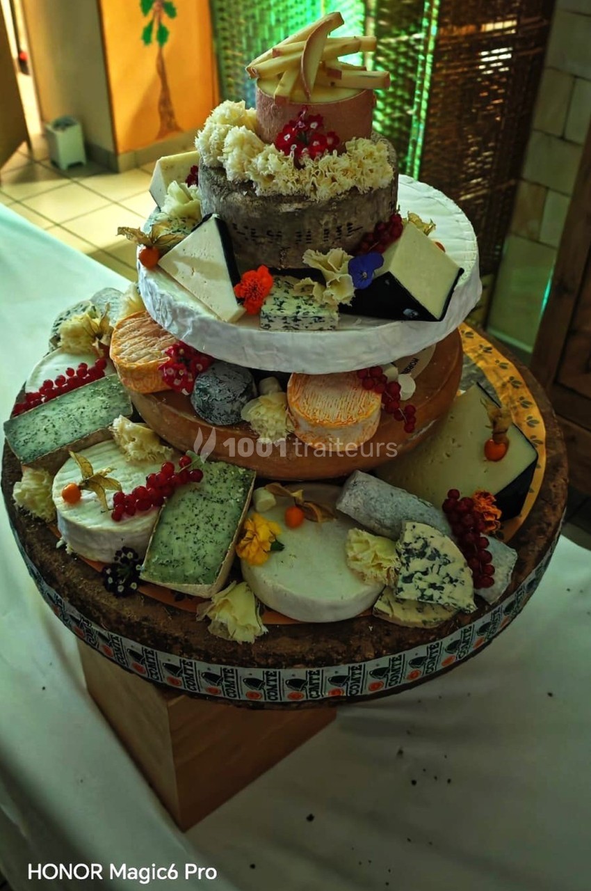 Plateau de fromages variés disposés en forme de pièce montée, décoré de fruits rouges et de fleurs comestibles.