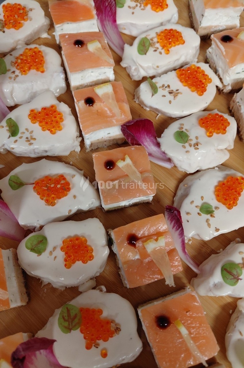 Assortiment de bouchées apéritives avec saumon fumé, œufs de poisson, crème et décorations florales.