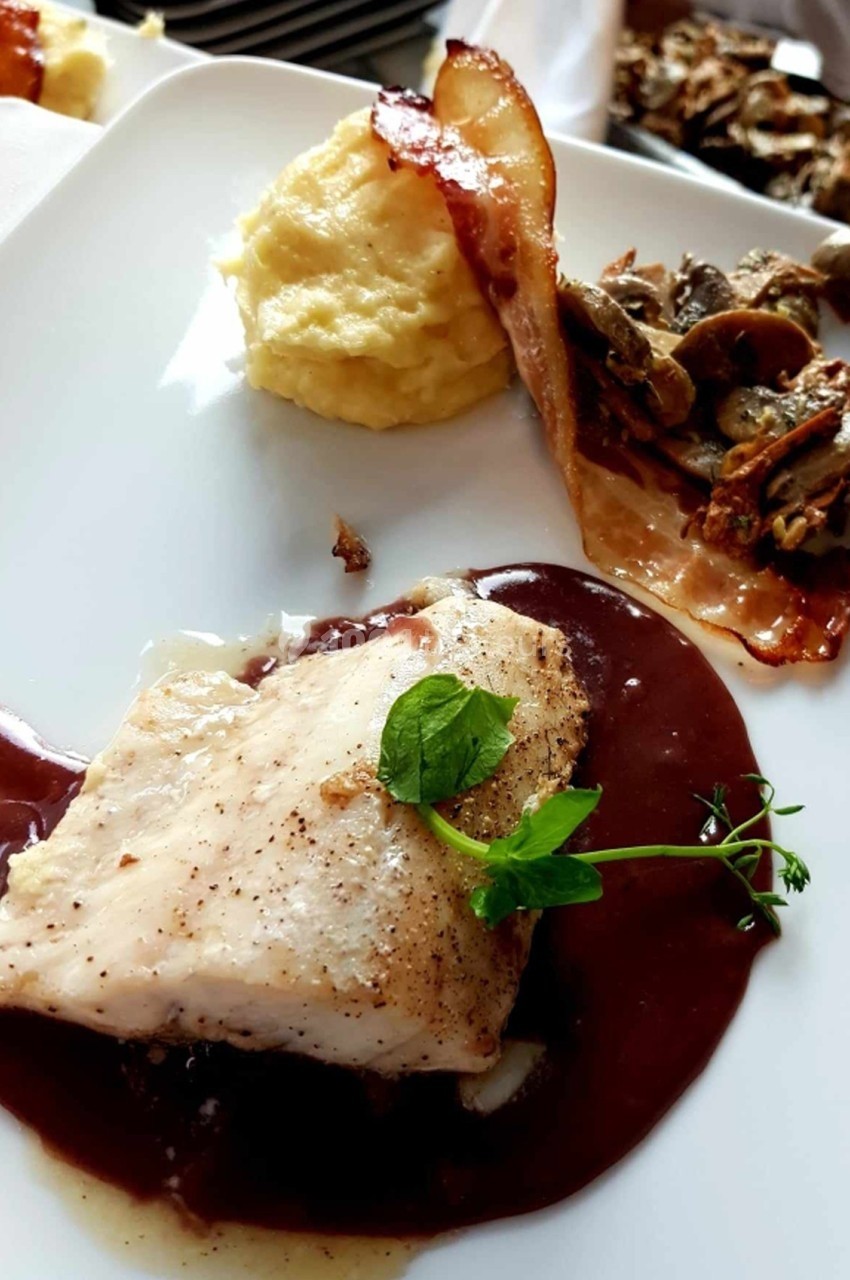 Filet de poisson nappé de sauce brune, accompagné de purée, lard croustillant et garniture de champignons.