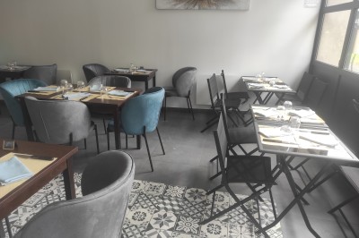 Salle de restaurant lumineuse avec tables dressées, chaises modernes et grandes fenêtres donnant sur un espace vert.