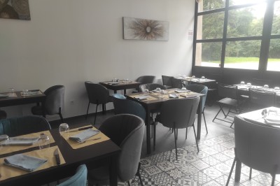 Salle de restaurant lumineuse avec tables dressées, chaises modernes et grandes fenêtres donnant sur un espace vert.