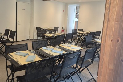 Salle de restaurant lumineuse avec tables dressées, chaises modernes et grandes fenêtres donnant sur un espace vert.