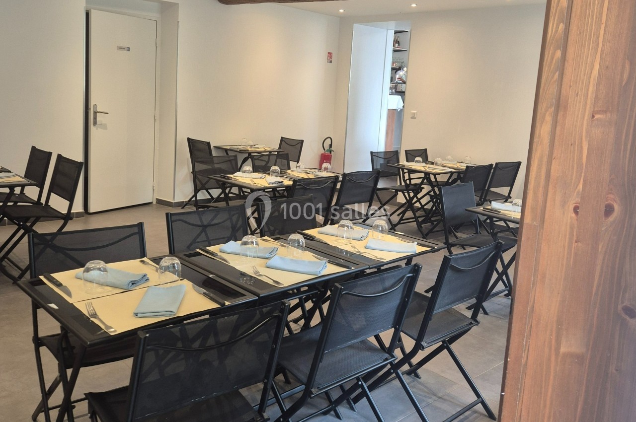 Salle de restaurant avec tables noires dressées, nappes jaunes, serviettes bleues et chaises pliantes noires.