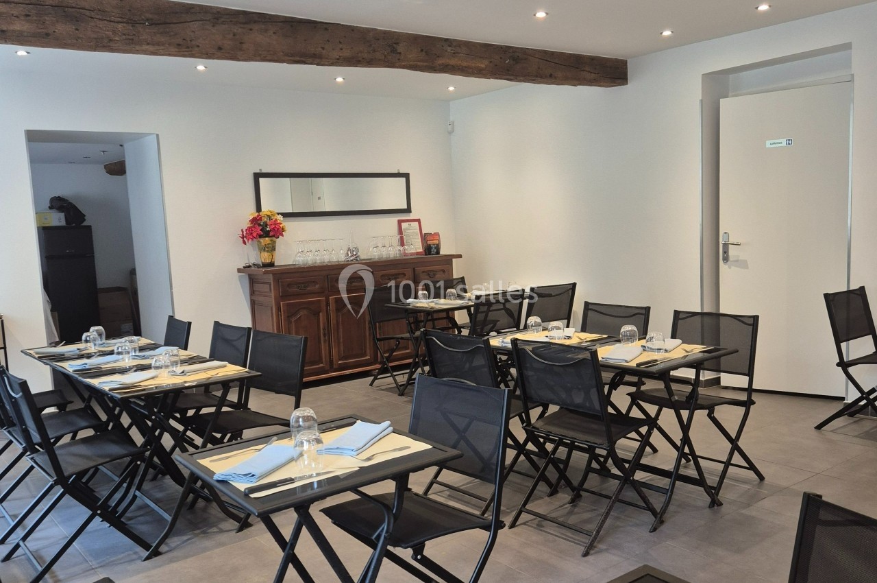 Salle de restaurant lumineuse avec tables noires dressées, chaises pliantes et un buffet en bois au fond.