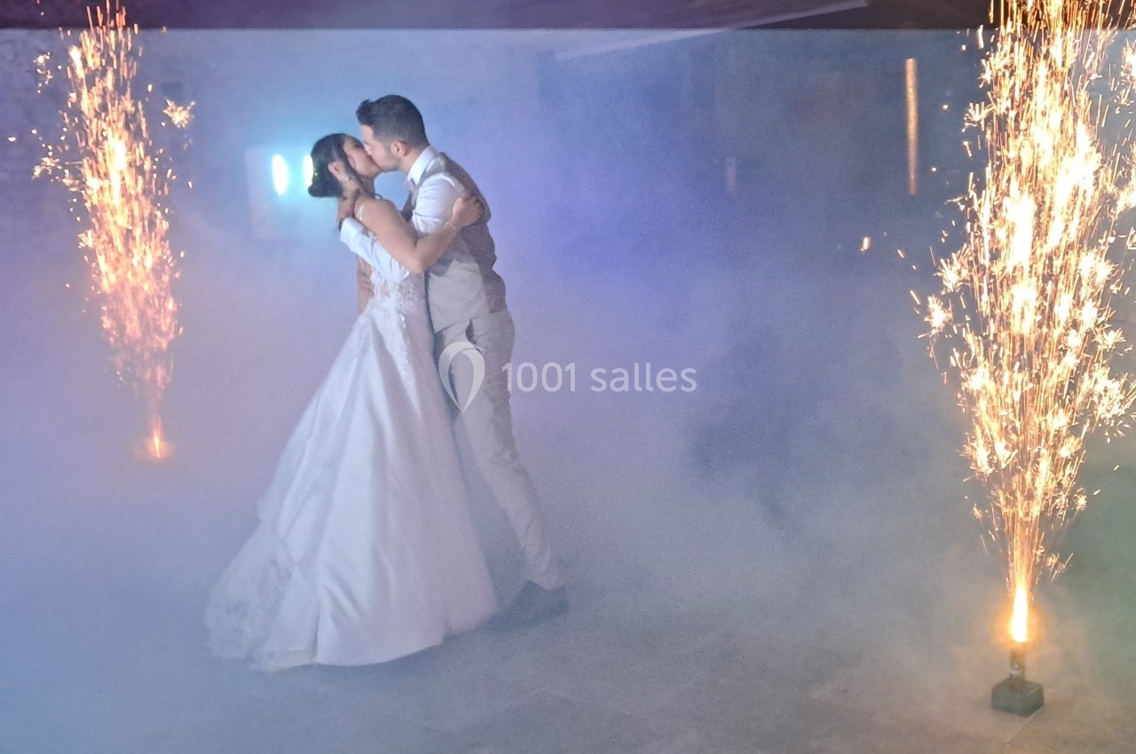 Un couple en tenue de mariage s'embrasse sur une piste entourée d'effets pyrotechniques et de fumée.