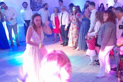 Un couple en tenue de mariage danse dans une salle éclairée par des lumières colorées et entourée de fumée.