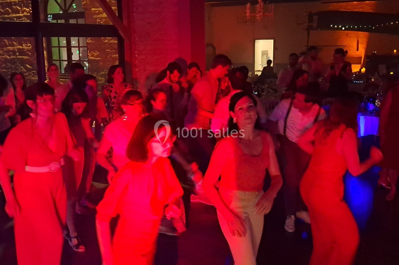 Des personnes dansent dans une salle faiblement éclairée avec des lumières rouges et une ambiance festive.