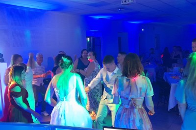 Un couple en tenue de mariage danse dans une salle éclairée par des lumières colorées et entourée de fumée.