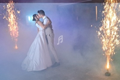 Un couple de mariés s'embrasse sur une piste de danse entourée de fumée et de fontaines d'étincelles.