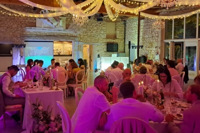 Salle de réception en pierre illuminée, décorée de guirlandes lumineuses et de fleurs, avec des invités dînant à table.