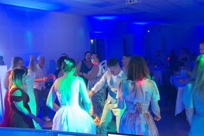 Des personnes dansent dans une salle éclairée par des lumières colorées, entourées de tables et de chaises.