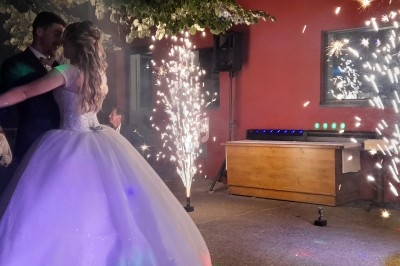 Un couple danse en tenue de mariage sous des étincelles lumineuses, dans un espace extérieur éclairé.