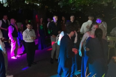 Groupe de personnes dansant et discutant lors d'une soirée en extérieur, éclairée par des lumières colorées.