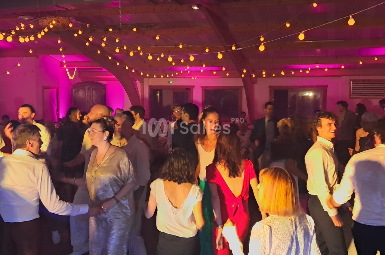 Des personnes dansent dans une salle éclairée par des guirlandes lumineuses et une lumière rose.