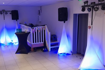 Homme debout devant un ordinateur portable, dans une salle éclairée par des lumières bleues, avec une projection en arrière…