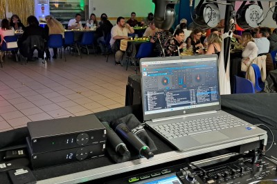 Homme debout devant un ordinateur portable, dans une salle éclairée par des lumières bleues, avec une projection en arrière…